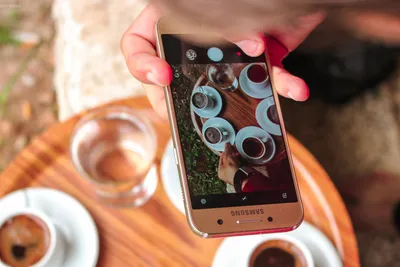 человек, держащий смартфон Samsung Galaxy, фотографирует свой кофе ·  Бесплатные стоковые фото