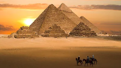 Обои на рабочий стол Египетские пирамиды, пустыня и люди на верблюдах на  фоне заходящего солнца и мужчин на лошадях, осматривающих завораживающую  панораму, обои для рабочего стола, скачать обои, обои бесплатно