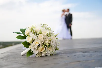 Свадебный букет лежит на дороге на фоне целующихся молодожёнов — Фото на аву